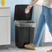 A person in jeans and shoes using a black Lavex step-on trash can in a kitchen.