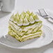 A piece of cake with green frosting next to a white cup of Matcha.Com matcha powder.