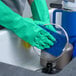 A pair of green heavy-duty unlined nitrile rubber gloves being used to wash dishes.
