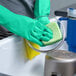 A pair of green heavy-duty unlined nitrile rubber gloves being used to wash dishes.
