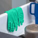 A pair of green heavy-duty unlined nitrile rubber gloves draped over the edge of a sink.