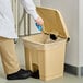 A person putting a plastic bag into a Lavex beige rectangular step-on trash can.