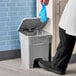 A person wearing blue gloves putting a glove in a Lavex rectangular step-on trash can with a plastic bag inside.