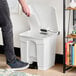 A person using a Lavex white rectangular step-on trash can.