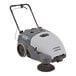 A grey and black Advance Terra 28B walk behind sweeper with a handle and wheels.