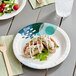 A Choice paper plate with a salad, raspberries, and almonds on a table.