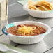 A bowl of chili with chips in a Choice white paper bowl on a table.