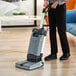 A person using an Advance SC100 upright floor scrubber on a hardwood floor.