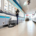 A woman using an Advance walk-behind floor scrubber to clean a grocery store aisle.