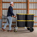 A man pushing a Gorilla hand truck with black containers on it.