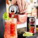 A person pouring Mr. & Mrs. T Bloody Mary Mix from a can into a glass with ice.