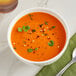 A bowl of orange soup with Judee's Heavy Cream Powder and spices next to a spoon.