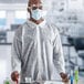 A man wearing a Cordova white polypropylene lab coat and face mask while holding a test tube.