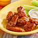 A plate of chicken wings and celery sticks with a yellow bowl of Tajin Mild Hot Sauce.