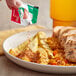 A person pouring Tajin Classic seasoning onto a plate of food.