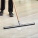 A person using a Lavex black double neoprene floor squeegee to clean a floor.