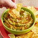 A hand dipping a chip into a bowl of guacamole with Tajin Habanero seasoning on the table.