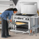 A woman putting food in a Wolf standard oven on a counter in a professional kitchen.