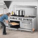 A woman putting a tray of food in a large Wolf stainless steel oven.