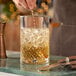 A 24 oz. diamond cut heavy-duty cocktail stirring and mixing glass filled with ice and a light-colored beverage.