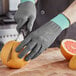 A person's gloved hand using a knife to cut an orange.