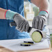A pair of gray cut-resistant food-safe gloves being worn while slicing an eggplant on a cutting board.
