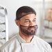 A man in a chef's uniform wearing a black nylon hairnet over his head.