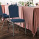 A table with a pink tablecloth and Lancaster Table & Seating navy fabric crown back stackable banquet chairs with blue cushions.