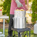 A man using a Choice aluminum stock pot with steamer basket and cover to cook corn outdoors.