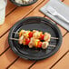 A black plastic plate with chicken skewers and vegetables on a table.