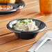 A black plastic Choice bowl filled with food on a table.