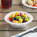 A bowl of fruit salad in a Choice white plastic bowl on a table.