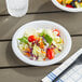 A Choice white plastic plate with salad and fruit on a table.