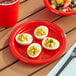 A red plastic plate with deviled eggs and fruit on a table.