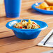 A blue plastic bowl filled with pasta and vegetables on a table.