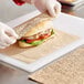 A person in gloves is wrapping a sandwich in Kraft deli wrap.