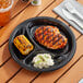 A Choice black plastic plate with food including chicken and corn on a table.