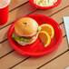A red Choice plastic plate with a burger and orange slices on a table.