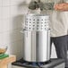 A man using gloves to hold a Choice aluminum stock pot with a steamer basket over a stove.