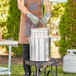 A man cooking food in a large aluminum pot on a grill.