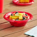 A red plastic bowl filled with fruit salad on a table.