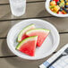 A white plastic plate with watermelon slices and fruit on a table with a fork.