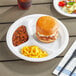 A Choice white plastic plate with a sandwich, beans, and mac and cheese on a table.