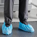 A person wearing blue Choice polypropylene shoe covers over shoes with anti-skid bottoms.