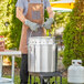 A man cooking food outside in a large aluminum stock pot with a steamer basket and cover.