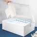 A hand opening a white Baker's Lane bakery box to reveal a cake with blue and white frosting.