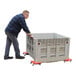 A man using a Vestil steel corner mover dolly to push a large plastic crate.
