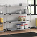 A Regency metal shelving unit in a professional kitchen holding yellow storage containers.