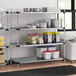 A Regency galvanized steel shelving unit in a professional kitchen with white and blue plastic bins on the shelves.