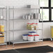 Stainless steel wire shelving unit with white and red plastic containers on the bottom shelf.